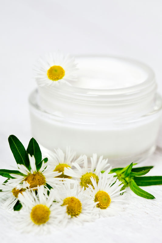 A jar of cream and some daisies on a white surface