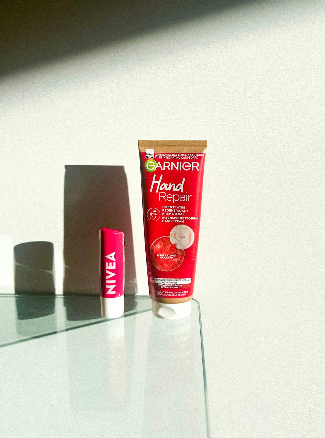 Garnier hand cream and nivea lip balm on glass table